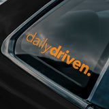 Orange 'dailydriven.' logo on a car window
