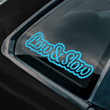 A blue decal saying "Low & Slow" shown on the window of a black car