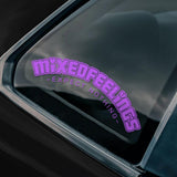Car window with a purple 'Mixed Feelings Expect Nothing' sticker and a logo at the bottom.