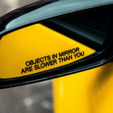 Yellow car mirror with 'Objects in mirror are slower than you' text