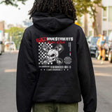 Person wearing a black hoodie with a graphic design on the back, standing on a street.