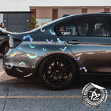 Black car with decorative stickers on a street, featuring a visible brand logo.