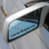 Car side mirror with 'EYES ON THE ROAD, FOOL' text reflection
