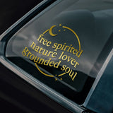 Car window with a gold decal reading 'free spirited nature lover grounded soul' on a black car.