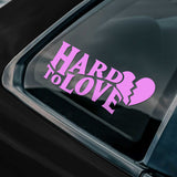 Pink 'Hard to Love' decal with a broken heart icon on a car window