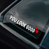 Car window with a sticker saying 'You Look Good' with hearts on a black car.