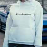 Female model wearing a white hooded sweater with “Bad Investments” cursive lettering design on it